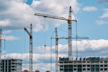 Bulutlu gökyüzünün arka planında endüstriyel vinçler. Turnalar ve yeni şehir bölgelerinin çok katlı binaları çekiliyor. İnşaat alanı arka planı. Kentsel alan.