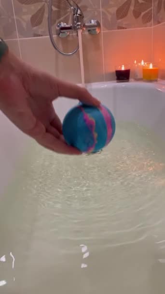 女人的手把一个冒泡的浴弹扔进浴缸里 用于水和皮肤护理中溶解的化妆品 一对夫妇浪漫的夜晚 温泉和放松的概念 — 图库视频影像