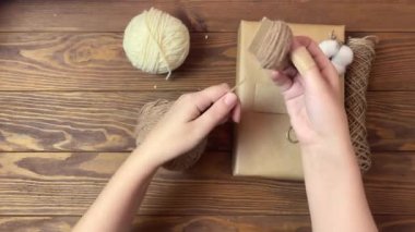 Kızlar kahverengi ipliği karton parçasının üzerine koyuyorlar. Noel ya da doğum günü hediyesi olarak el yapımı el yapımı süslemeler. Sandık ambalaj kağıdı, sicim, pamuk ve makas ahşap masada. Şenlik havası.