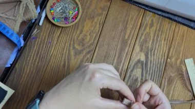 Kadın parmaklarının üst görüntüsü kayışı beyaz metal bir sürgüye bağlıyor. Terzi, eko-deriden yapılmış bir ürün ya da aksesuar diker. Ahşap bir masada çalışma akışı. Hobi ya da el yapımı konsept.