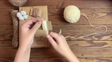 Kızlar beyaz ipliği bir karton parçasına geçirir. Sandık ambalaj kağıdı, sicim, pamuk ve makas ahşap masada. Şenlik havası. Noel veya doğum günü hediyesi olarak el yapımı el yapımı süslemeler.