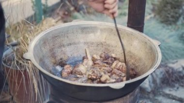 Şef büyük kazanda kızartılmış eti slotlu kaşıkla karıştırıyor. Kaynar yağda kızarmış biftek. Turistler doğada kamp yapar. Tavada kamp yemeği pişirmek..