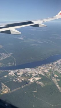 Wing of aircraft above landscape of city with blue sky. View from window of plane. Feeling of freedom. Airplane flight. Traveling on fastest and safest means of transport.