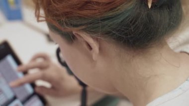 Girl with colored hair touching scroll page app on tablet. Woman is looking for interesting pictures on device. Close up female using smartphone.