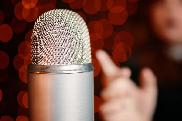 Close-up of vintage disco microphone and silhouette of female singer on bokeh background. Woman pulls hand to microphone for sing at concert. Night party in club or restaurant.