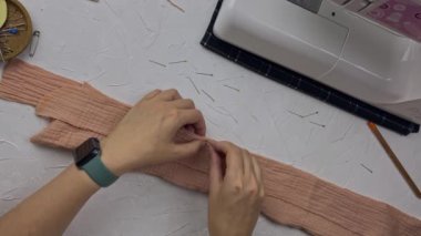 Top view of fashion designer workplace. Seamstresss hands try on details of shirt collar with pin. Woman sews clothes from cotton muslin. Sewing machine and tools on white table.