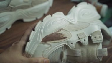 Artist paints white sneakers on wooden table. Brush with brown acrylic paint. Design of sports shoes. Handmade, crafts, leisure and hobby.
