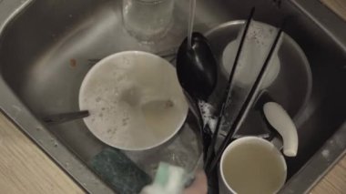 Mans hands washing tableware with water. Close-up of a sink with dirty dishes after a family supper. Domestic cleanliness and hygiene. Household chores.