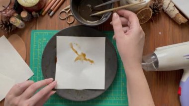 Females hands paint with brush and dipping piece of paper into plate of instant coffee. Hairdryer, pencils and other objects on wooden table. Design and decorating paper for scrapbooking.