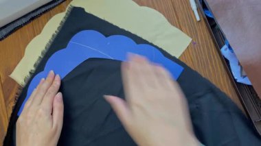 Needlewoman outlines the plastic shape of the tiara on the fabric. Womens hands create an ethnic hair accessory. Eco-leather and sewing tools on a wooden table. Hobbies and crafts.