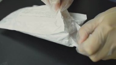 Persons hands in gloves take out of white paper bag parcel wrapped in bubble wrap. Delivery and unpacking of online purchases.