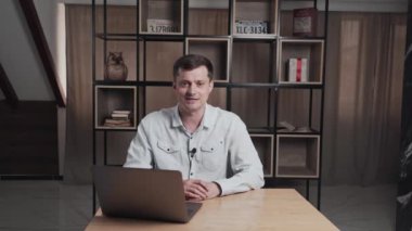 Man gives an interview sitting at a table with a laptop. Person speaks and stopped. Unsuccessful duplicates.