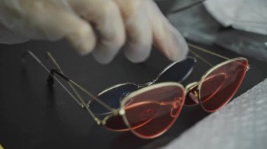 Womens gloved hands put set of sunglasses with colored lenses on table. Fashion accessories demonstration. New glasses, bubble wrap and stylish eyewear on desktop. Online buy.