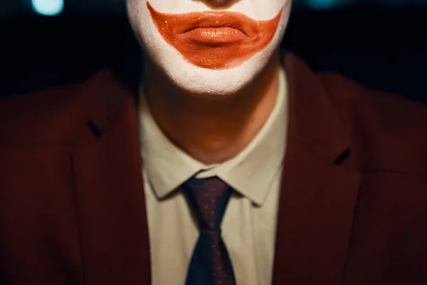 Close-up of a guys mouth with joker makeup. Man in a suit and tie. Halloween party.