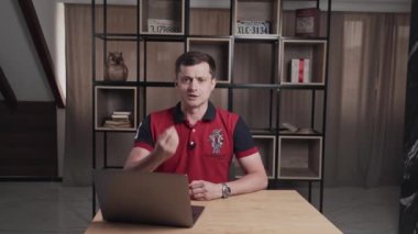 Spor eğitimi ve bilişsel kanal jestlerini elleriyle sunan ve konuşan. Masada dizüstü bilgisayarlı bir adam kameraya bakarak bir şey söylüyor. Televizyonda program röportajı ya da yayını.