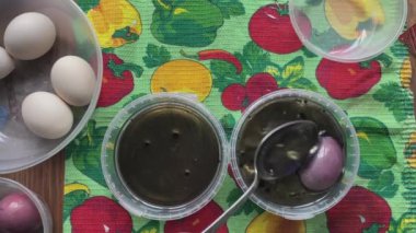 İnsanlar Paskalya yumurtalarını boyarlar. Kadın yumurtayı kaşığa koyar ve sırayla sıvı boya kutularına batırır. Bahar tatili için hazırlık. Sanat derslerinin en üst görünümü.