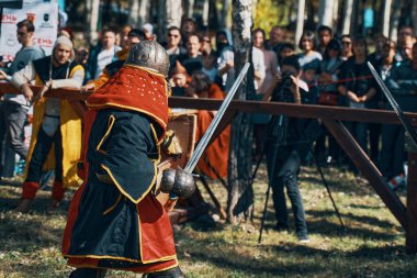 Kırmızı ve siyah cübbeli bir savaşçı ve bir kask. Ortaçağ kültürünün festivali. Mızrak dövüşü turnuvalarının taklidi. Seyircilerle dolu bir arena. Bishkek, Kırgızistan - 13 Ekim 2019