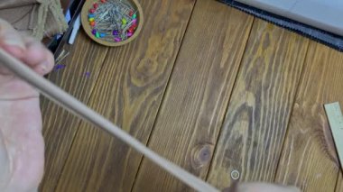 Düz kadın parmakları, kayışı beyaz metal bir sürgüye bağlıyor. Terzi, eko-deriden yapılmış bir ürün ya da aksesuar diker. Ahşap bir masada çalışma akışı. Hobi ya da el yapımı konsept.