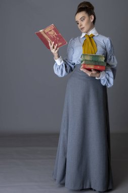 Çizgili pamuklu bluz, hardal sarısı kravat ve gri etek giyen Edwardlı işçi sınıfı bir kadın stüdyo arka planına karşı yürüyor ve elinde kitaplar var.