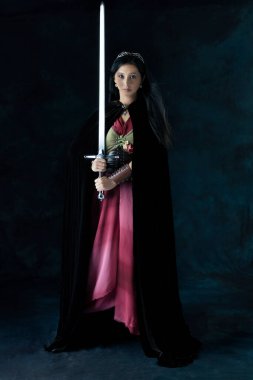 Bir elf (veya diğer fantezi karakteri) bağcıklı korse, kadife pelerin ve etek giyen ve kılıç tutan savaşçı bir kadın.