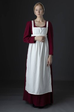 Kırmızı keten elbise giyen, önlüklü ve şapkalı bir hizmetli stüdyo arkaplanına yaslanmış.