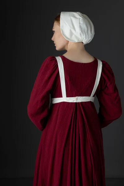 スタジオを背景にエプロンとキャップ付きの赤いリネンのドレスを着たリージェンシーメイド — ストック写真