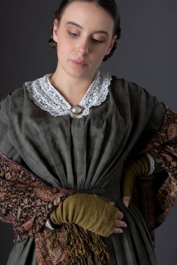 Koyu yeşil korse ve şal desenli etek giyen Viktorya dönemi işçi sınıfı bir kadın.