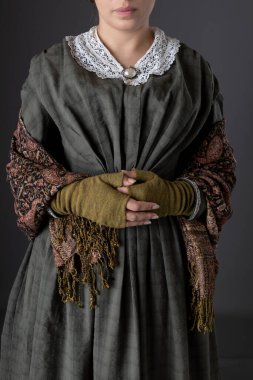 Koyu yeşil korse ve şal desenli etek giyen Viktorya dönemi işçi sınıfı bir kadın.