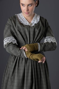 Koyu yeşil giyen Viktoryan bir kadın gri bir stüdyo arka planına dantel yakalı bir korse ve bluz giymişti.