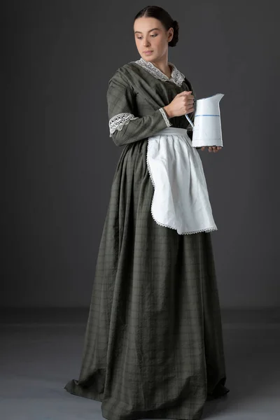 女佣人维多利亚时代的女佣或工人阶级妇女 身穿深绿色的格子格子裙和短裙 手持壶 — 图库照片