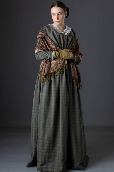 A Victorian working class woman wearing a dark green bodice and skirt with a paisley shawl