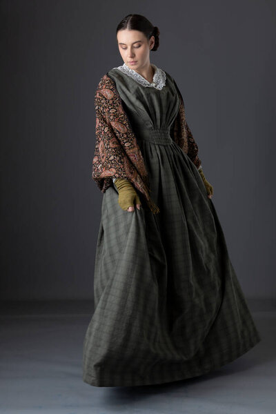 A Victorian working class woman wearing a dark green bodice and skirt with a paisley shawl
