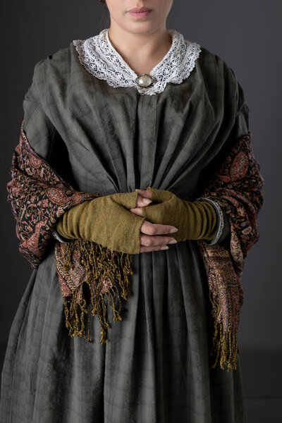 A Victorian working class woman wearing a dark green bodice and skirt with a paisley shawl