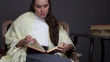 A Victorian or Edwardian woman sitting in a  chair reading a book.