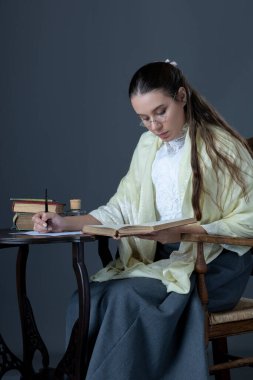 A Victorian or Edwardian woman sitting at a desk writing with an ink dip pen
