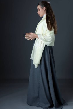 Victoria döneminden ya da Edwardlı bir kadın elinde bir yığın kitapla stüdyonun arka planına karşı duruyormuş.