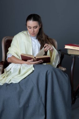 A Victorian or Edwardian woman sitting in a chair and reading a book