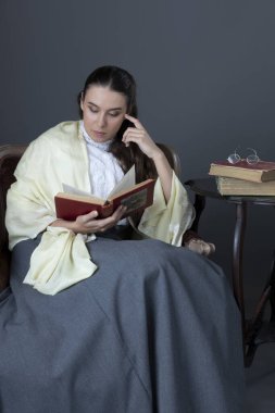 A Victorian or Edwardian woman sitting in a chair and reading a book