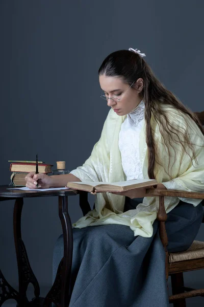 A Victorian or Edwardian woman sitting at a desk writing with an ink dip pen