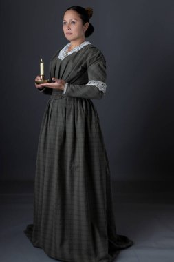 Victoria dönemi işçi sınıfı bir kadın karanlıkta elinde mumla tek başına ayakta duruyor.