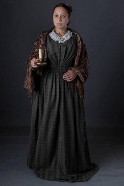 Victoria dönemi işçi sınıfı bir kadın karanlıkta elinde mumla tek başına ayakta duruyor.