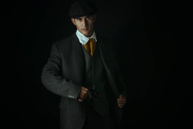 Siyah bir zemine karşı tek başına duran işçi sınıfı Viktorya Dönemi 'nden bir adam. Gangster olabilir.