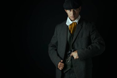 Siyah bir zemine karşı tek başına duran işçi sınıfı Viktorya Dönemi 'nden bir adam. Gangster olabilir.