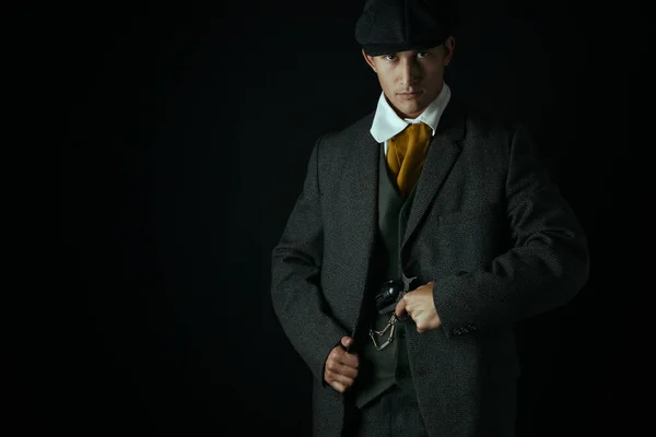 A working class Victorian man standing alone against a black backdrop. He may be a gangster