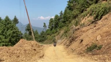 Lalitpur, Nepal - 12 Ekim 2021: Arka planda Himalaya Dağları olan dağlarda toprak bir yolda motosiklet sürmek.