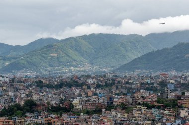 Katmandu şehrindeki nüfus yoğunluğunun fırtınalı bir gökyüzünün altında iniş için gelen bir uçakla görüntüsü..