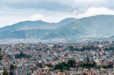 Katmandu şehrindeki nüfus yoğunluğunun fırtınalı bir gökyüzünün altında iniş için gelen bir uçakla görüntüsü..