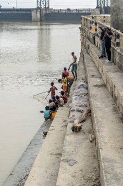 Koshi, Nepal - 22 Ekim 2021: Arkaplanda Koshi Nehri Baraj Köprüsü ile balık tutan çocuklar.