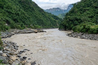Ağaçlarla kaplı tepeler arasındaki vadide taşlarla kaplı bir nehir..
