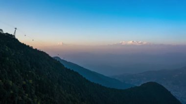 Güneş Himalaya Dağları 'nın üzerinden batıyor ve bir teleferik ön planda dağdan inip çıkıyor..